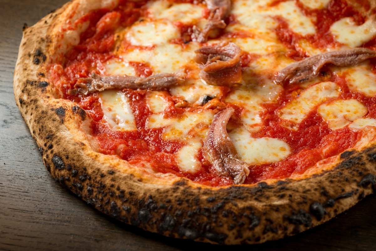 This photo shows a pizza with tomato, mozzarella and anchovies.