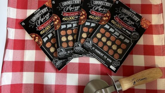 This photo shows four lottery scratch-off tickets on a red-checkered tablecloth next to a pizza slicer.