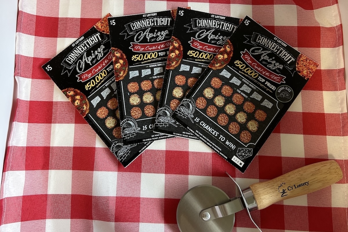 This photo shows four lottery scratch-off tickets on a red-checkered tablecloth next to a pizza slicer.
