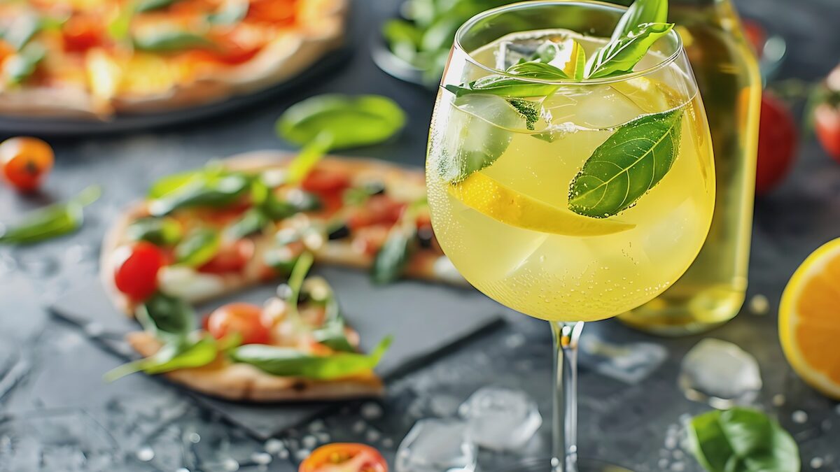 This photo shows a Limoncello spritz drink at a table with pizza and antipasti in the background.