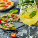 This photo shows a Limoncello spritz drink at a table with pizza and antipasti in the background.