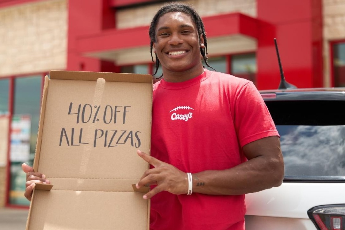 This photo shows a man in a red Casey's t-shirt holding an empty pizza box with words on the inside lid: "40% Off All Pizzas."