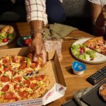 This photo shows a man's hand removing a slice from a whole Domino's pizza.