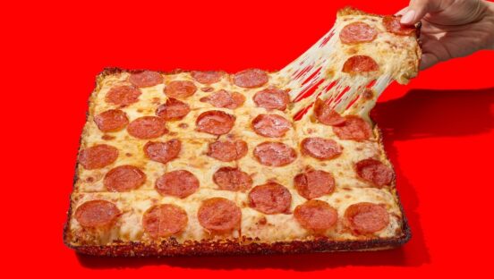 This photo shows a hand pulling a slice of Casey's pepperoni and cheese pan pizza from a whole pie.