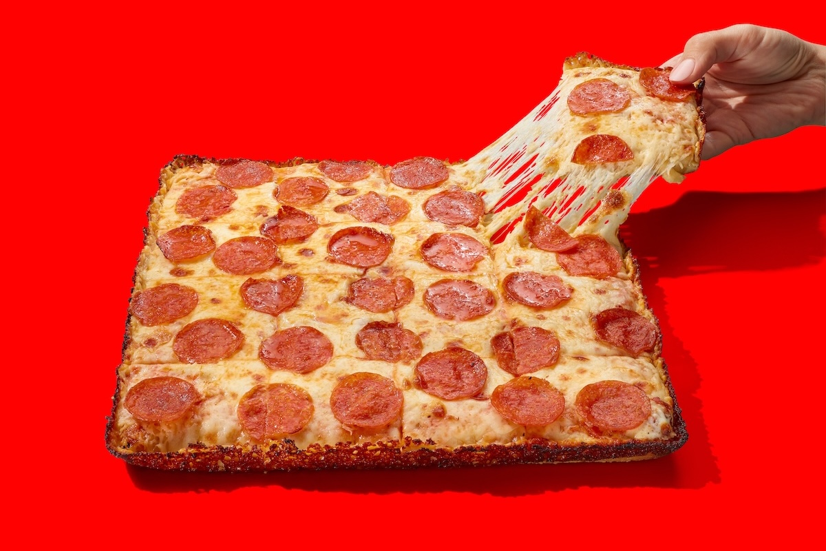 This photo shows a hand pulling a slice of Casey's pepperoni and cheese pan pizza from a whole pie.