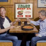 This photo shows two men seated at a Lou Malnati's booth, laughing and sharing a deep-dish pizza.