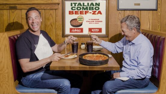 This photo shows two men seated at a Lou Malnati's booth, laughing and sharing a deep-dish pizza.