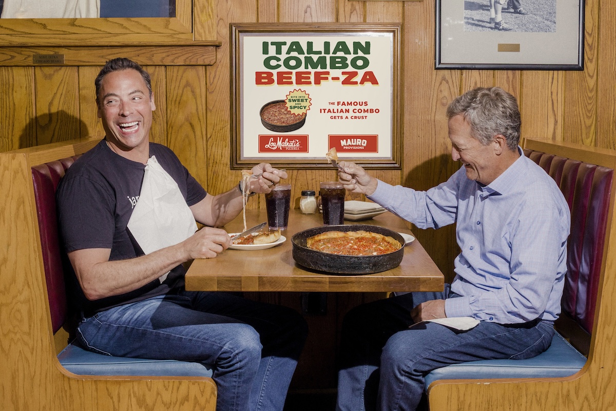 This photo shows two men seated at a Lou Malnati's booth, laughing and sharing a deep-dish pizza.