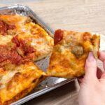 This photo shows a woman's hand holding a slice of sausage pizza that she just pulled from a whole pie.
