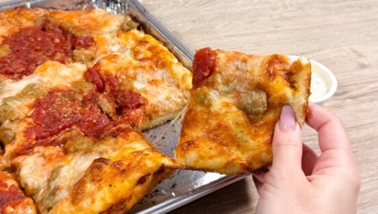 This photo shows a woman's hand holding a slice of sausage pizza that she just pulled from a whole pie.