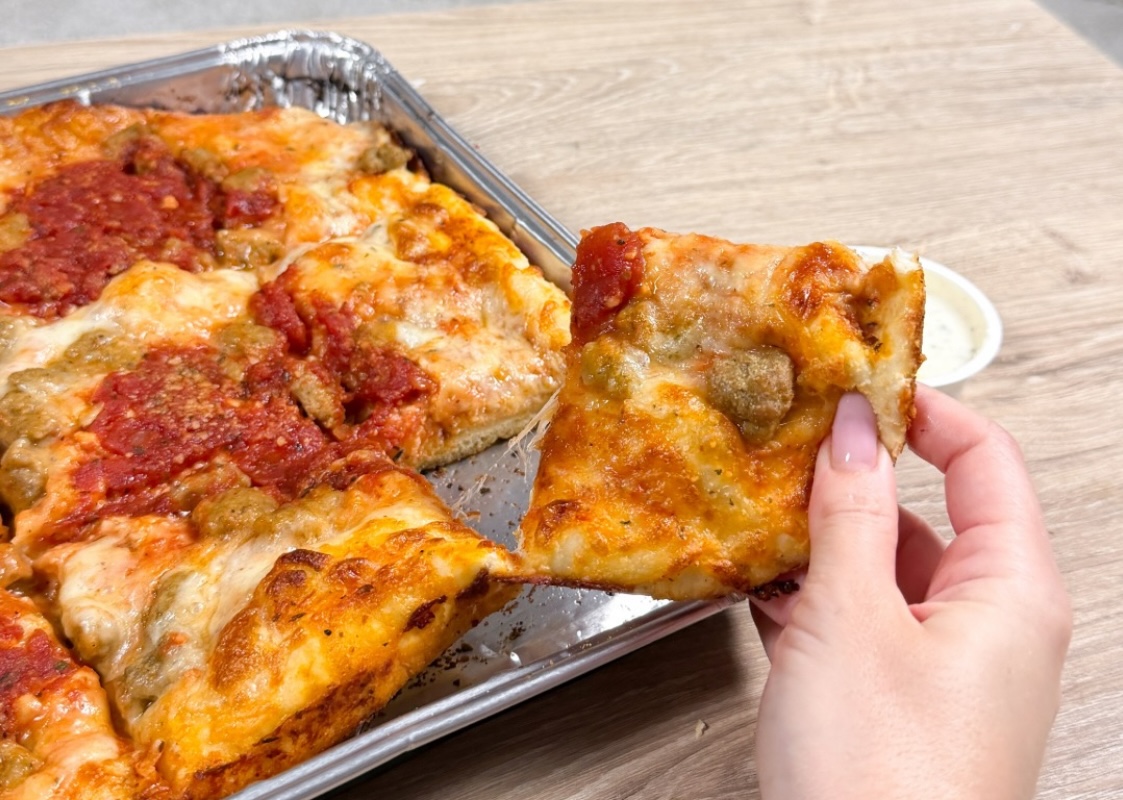 This photo shows a woman's hand holding a slice of sausage pizza that she just pulled from a whole pie.