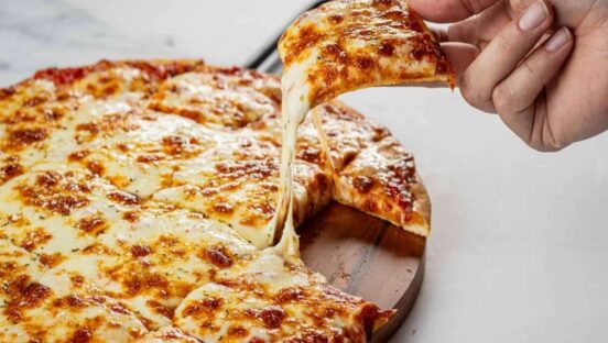 This photo shows a woman's hand removing a slice from a whole cheese pizza.